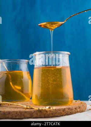 Fresh honey dripping glass pot cork coasters against blue background Stock Photo