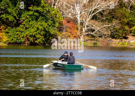 A couple row a wooden boat in the great pond of New York City Central Park in the fall among the beautiful Autumn colored trees. Stock Photo