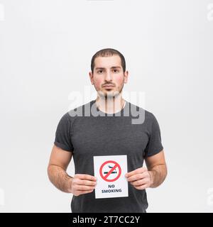 Portrait young woman holding no smoking sign against white background Stock Photo