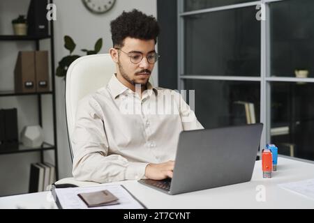 Young businessman sitting at his workplace and working on laptop in visa center Stock Photo