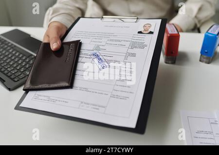 Close-up of specialist giving approved visa documents to tourist in office Stock Photo