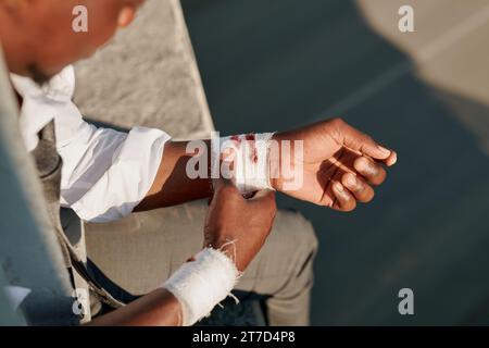 High angle view of depressed man with bandaged wrists sitting on the edge of bridge Stock Photo