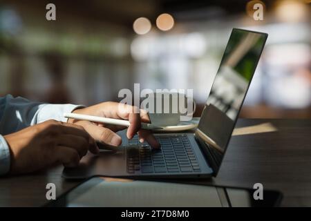 man Working using a laptop computer, sitting at a table, typing on the notebook keyboard workspace, and business technology Stock Photo