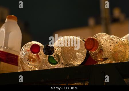 Multiple plastic beverage containers lie flat on top of a recycling bin covered with rain drops. Stock Photo