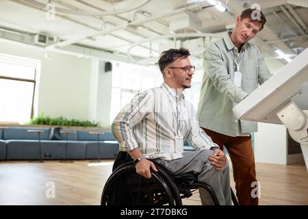 Young businessman helping man with disability using assistant computer Stock Photo