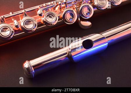 Detail of metal flute head and body on black table with red and blue lights. Elevated view. Stock Photo