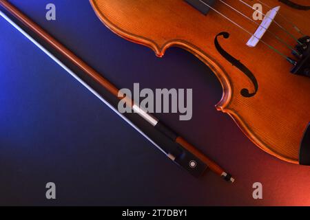 Detail of traditional stringed violin body and bow on black background with red and blue lights. Top view. Stock Photo