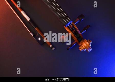 Detail of violin headstock and bow on black background with red and blue lights. Top view. Stock Photo