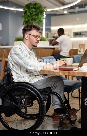 Vertical image of man with disability sitting in coffee shop and working online on laptop Stock Photo
