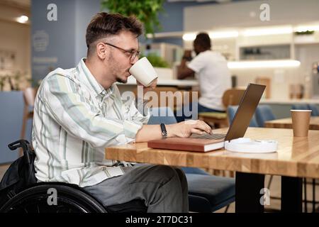 Young businessman with disability drinking coffee while working online in cafe Stock Photo