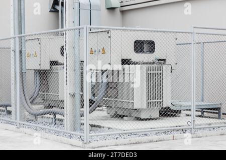 Electricity transformer high voltage Three phase electric power with safety area fence protection zone in industry building. Stock Photo