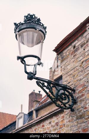An old-style wrought iron street lamp on the brick wall of a house during the day. Stock Photo