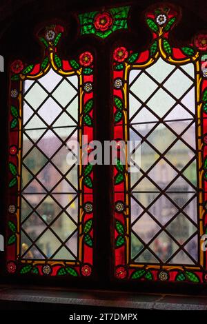 Beautiful colorful medieval stained glass window. Flower motifs. The bustle of the city in the background. Stock Photo