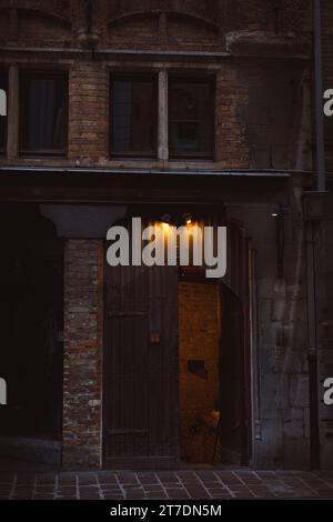 A large medieval-style wooden door, reminiscent of a castle entrance, in mystical lighting. Brick wall building. Stock Photo