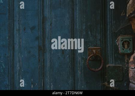 A weathered old blue wooden front door with a rusty round knocker and lock. Stock Photo