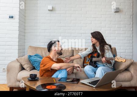 Young creative couple, freelancers web designers taking a break having fun playing electric guitar listening music in their apartment home office list Stock Photo