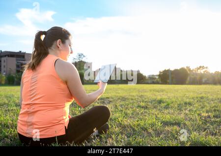 Rear view of young woman using tablet in park with beautiful sky Stock Photo