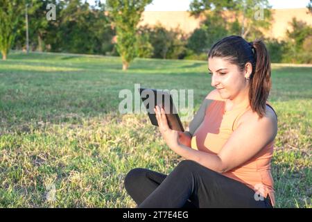 Young Caucasian woman smiling and happy using tablet sitting in park Stock Photo