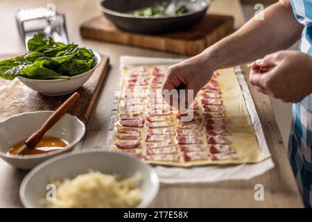 The cook prepares mini pizza cakes, puts pieces of bacon on puff pastry. Recipe procedure: 2 of 10 Stock Photo