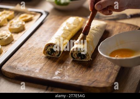 The cook brushes an egg onto a puff pastry roll. Recipe procedure: 7 of 10 Stock Photo