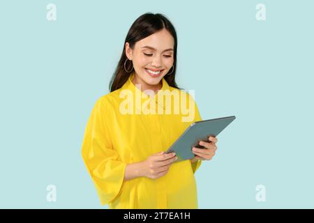 Cheerful young woman using digital tablet on blue Stock Photo