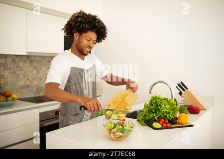 African American man in apron prepares vegetarian salad at kitchen Stock Photo
