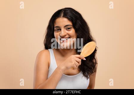 Smiling beautiful indian woman brushing her thick curly hair with bamboo comb Stock Photo
