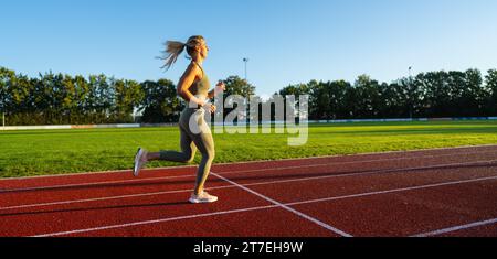 Female athlete running on a sunny track field Stock Photo