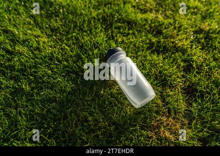 Water bottle lying on the grass in sunlight. Sports gear concept image Stock Photo