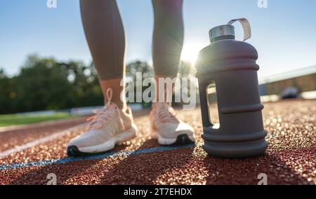 Close-up of a large water bottle on a running track with woman's legs in background Stock Photo