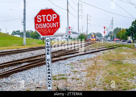NEW ORLEANS, LA, USA - NOVEMBER 11, 2023: Stop Dismount Close Clearance sign next to the railroad tracks with an oncoming train in the distance Stock Photo