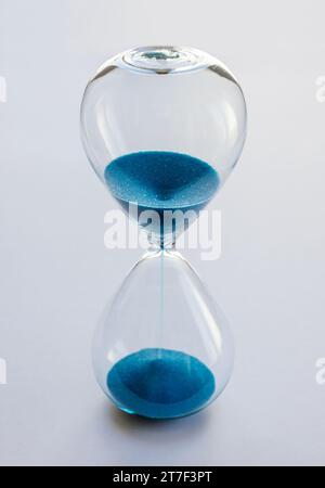 Hourglass containing blue sand isolated on white background. Concept of time passing Stock Photo