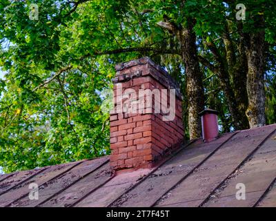 Old brick chimney in need of repair on a roof. Heating and fire safety concept Stock Photo