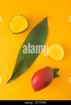 Fresh red mango and two halves and large leaf on yellow background.Top view. Stock Photo