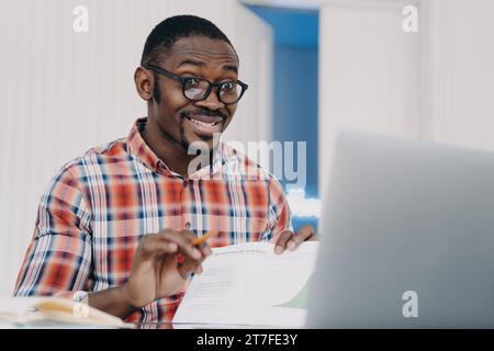 Confident Black man in glasses making a video call on his laptop, engaged Stock Photo