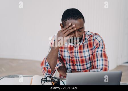 Exhausted Black man with hand on forehead stressing over work at laptop Stock Photo