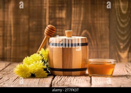 Honey in a small wooden barrel and a transparent glass bowl, a wooden dipper, yellow flowers on an aged wooden background, close-up. Stock Photo