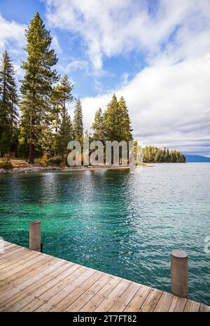 Clear blue-green lake water with a dock and pine trees on a sunny day in Lake Tahoe, California, USA Stock Photo