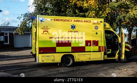 Bright yellow emergency Dublin Fire Brigade ambulance with open doors parked under autumn trees, ready for urgent medical services. Stock Photo