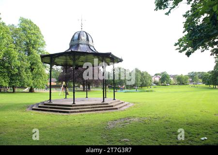 old fashioned band stand in the public park with grass, trees and houses in view. Stock Photo