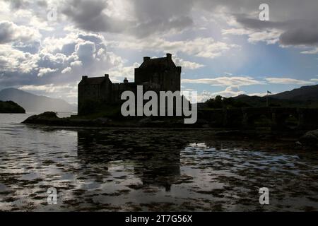 silhouetted eilean donan castle in scotland with reflection on the river and the the sun going down. Stock Photo