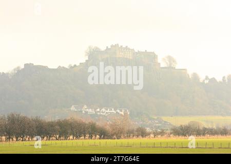 stirling castle in the distance on a hazy day with field, trees and houses in the foreground. Stock Photo