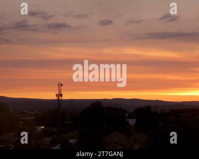 sun setting over the hills with tv antenna and hills silhouetted against an orange and yellow cloudy sky Stock Photo
