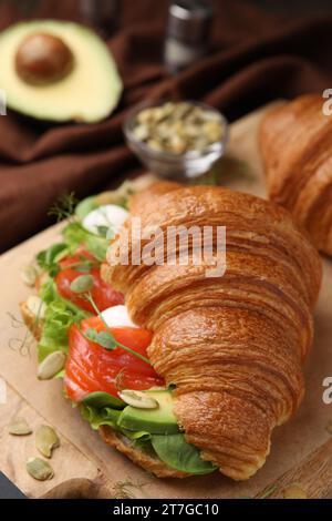 Tasty croissant with salmon, avocado, mozzarella and lettuce on table, closeup Stock Photo