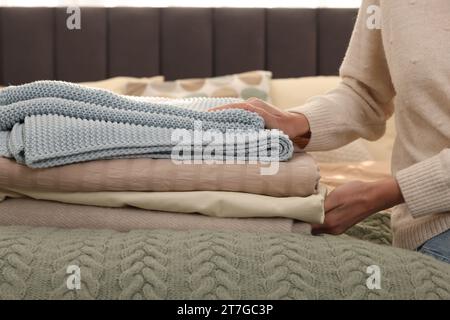 Woman with stack of different folded blankets on bed, closeup. Home textile Stock Photo