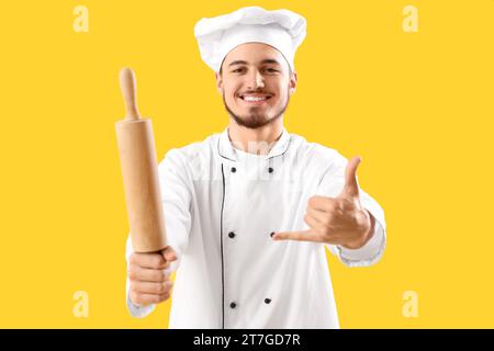 Male chef with rolling pin showing 'call me' gesture on yellow background Stock Photo