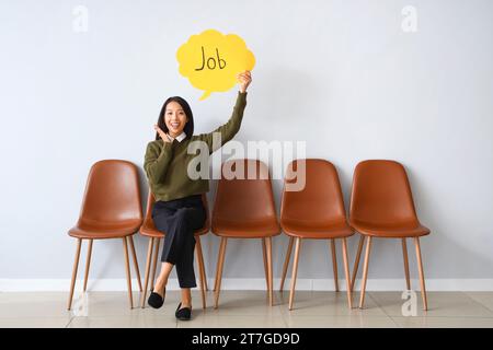 Asian businesswoman holding speech bubble with word JOB near light wall Stock Photo