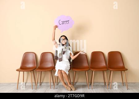 Asian businesswoman holding speech bubble with word CAREER near beige wall Stock Photo