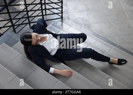 Woman fallen down stairs suffering from pain in back, above view Stock Photo