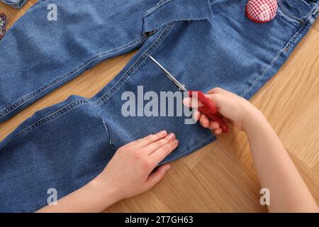 Woman cutting jeans with scissors at wooden table, above view Stock Photo